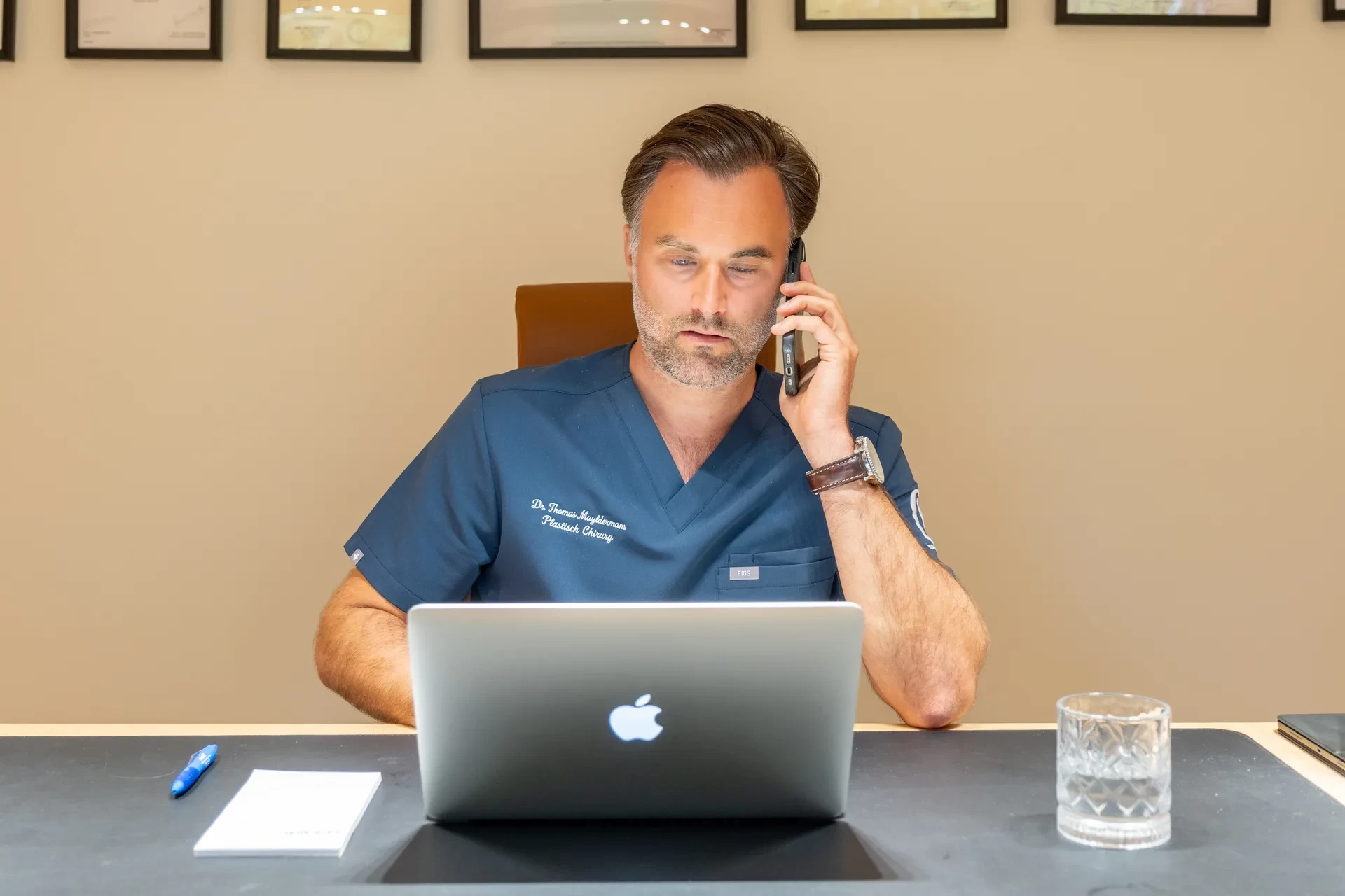 Dr. Muyldermans voert een telefonisch consult uit aan zijn bureau.